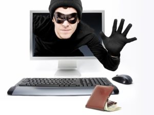 a cyber thief or criminal in a mask peering from the computer screen to scam and steal your identity.